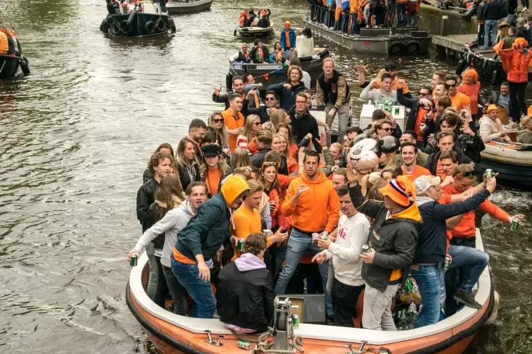 Een realistische sfeerfoto van het centrum van Drachten op Koningsdag, met feestelijke drukte, winkels en een levendige oranjesfeer.